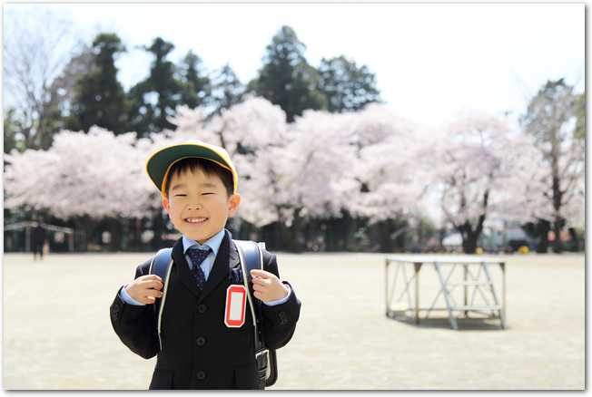 ランドセルを背負って桜の並木を背景にうれしそうな男の子
